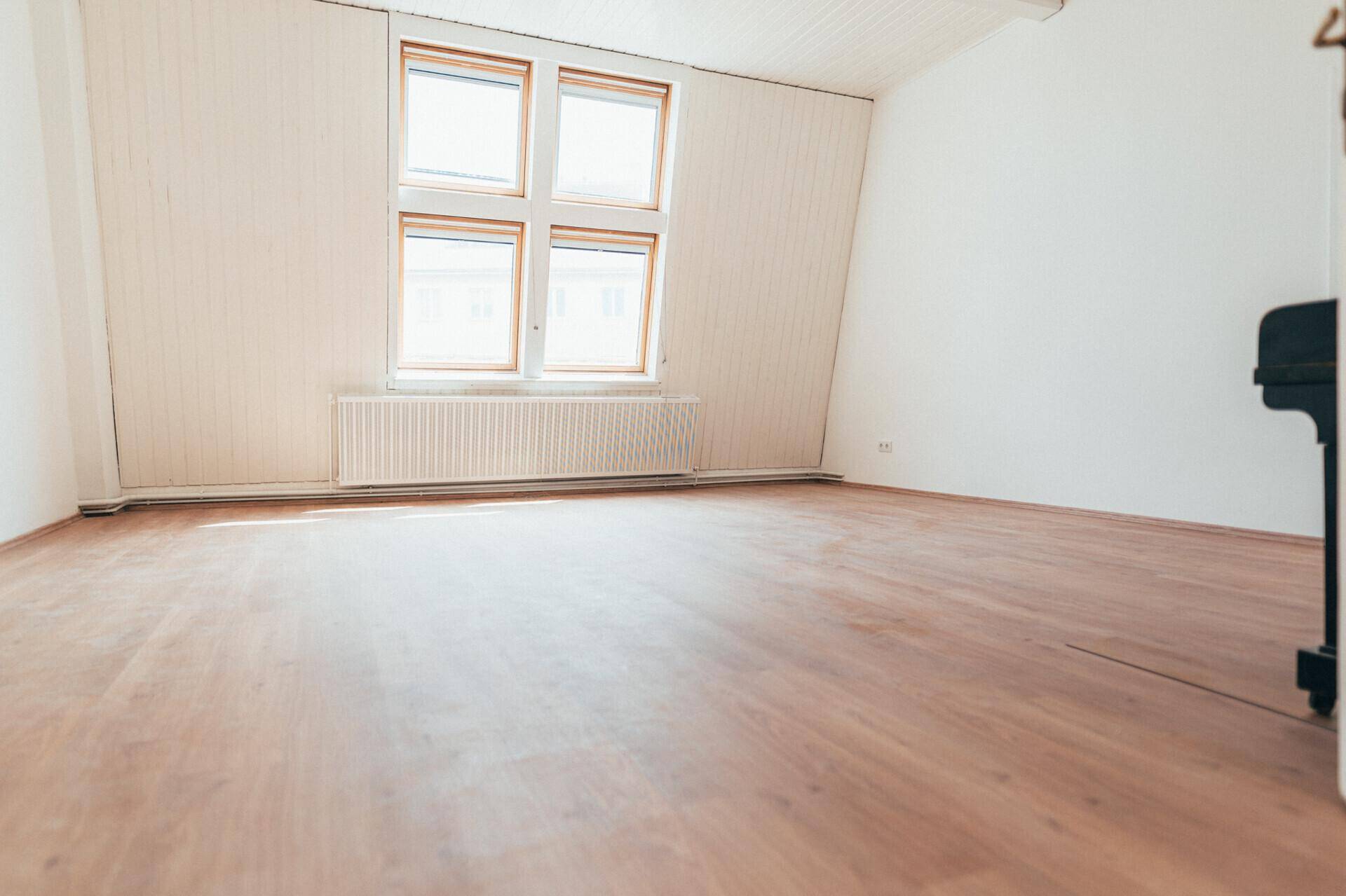 Heller, leerer Raum mit Laminatboden, weißen Wänden und einem großen Fenster, bereit zur Einrichtung.