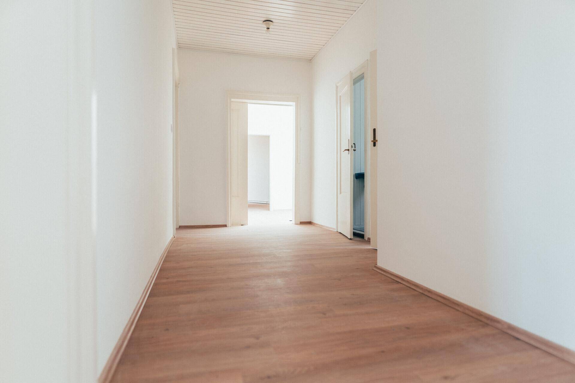 Langer, heller Flur mit Laminatboden und weißen Wänden, der mehrere Türen zu anderen Zimmern verbindet.