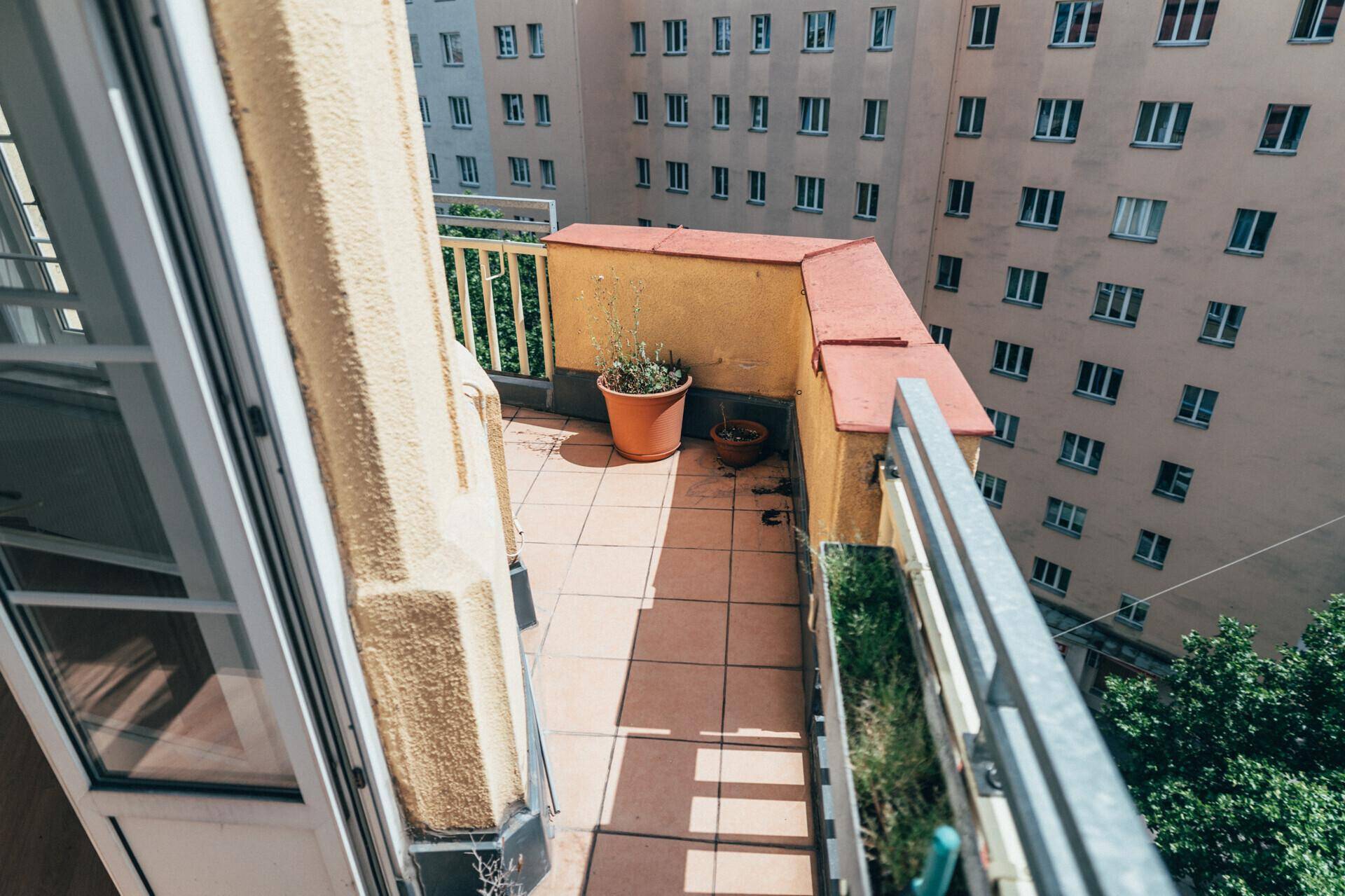 Kleiner Balkon mit Fliesenboden und Topfpflanzen, bietet einen Blick auf umliegende Gebäude.
