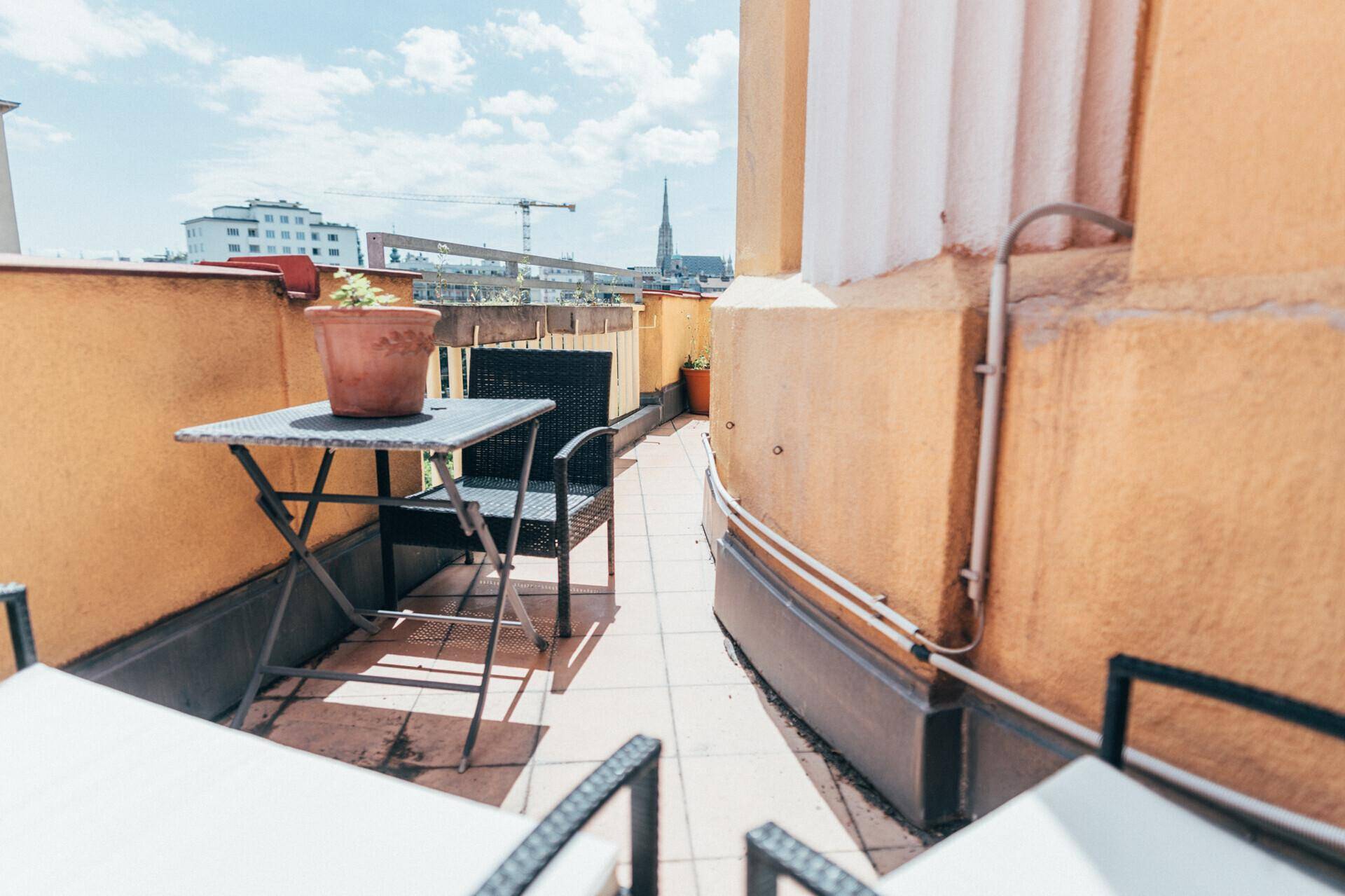 Sonniger Balkon mit Fliesenboden und Gartenmöbeln, bietet einen weiten Blick über die Stadt.