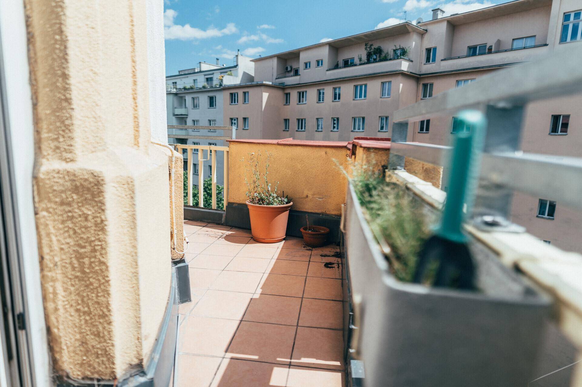 Kleiner Balkon mit Fliesenboden und Topfpflanzen, bietet einen Blick auf umliegende Gebäude.