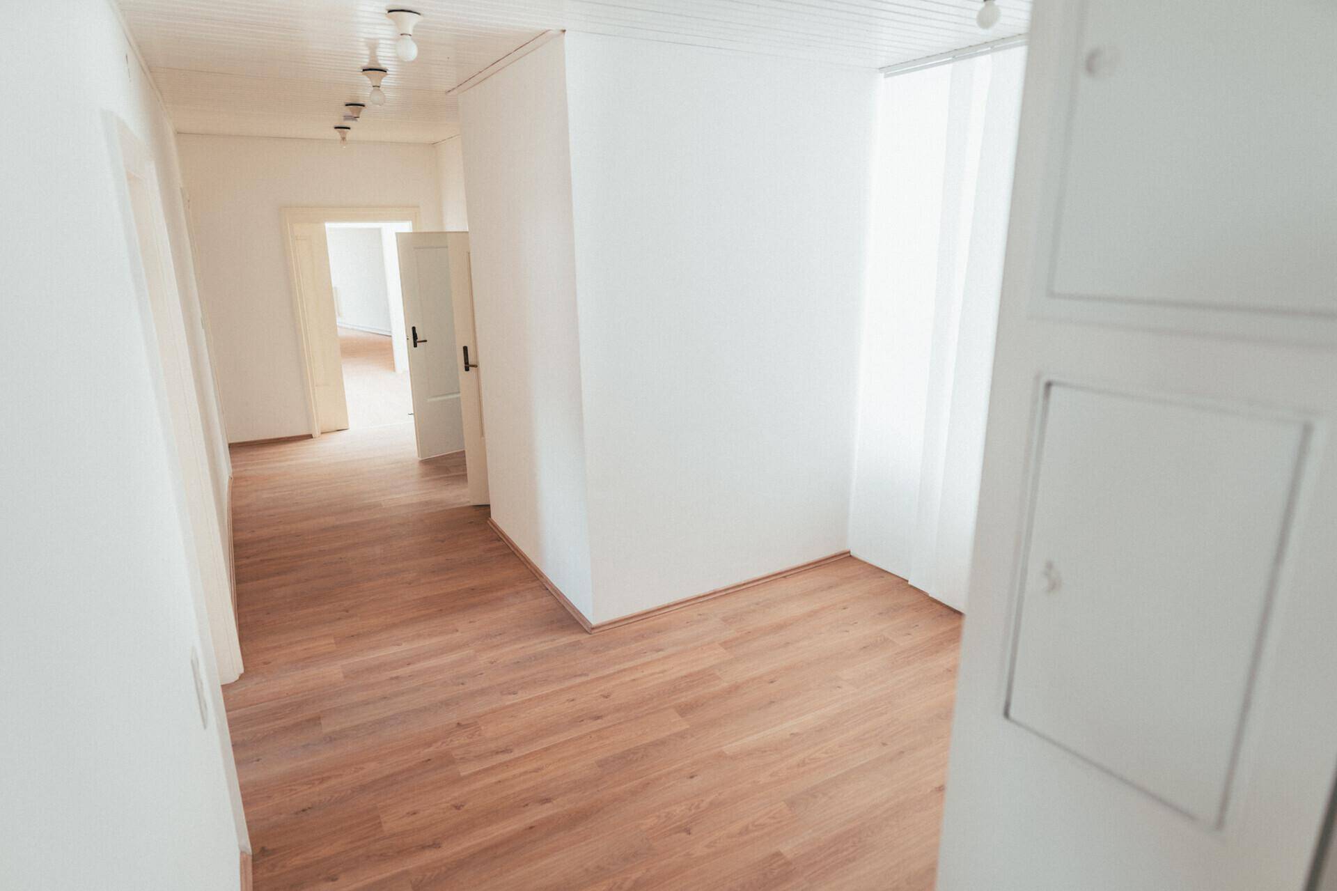 Heller Flur mit Laminatboden, weißen Wänden und Deckenstrahlern, der zu weiteren Räumen führt.