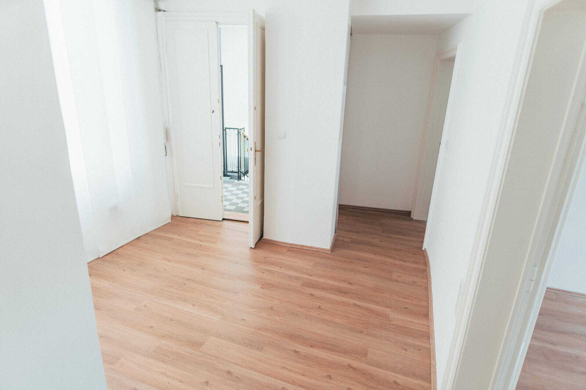 Geräumiger, heller Raum mit Laminatboden und weißen Wänden, offene Türen zu einem weiteren Zimmer.