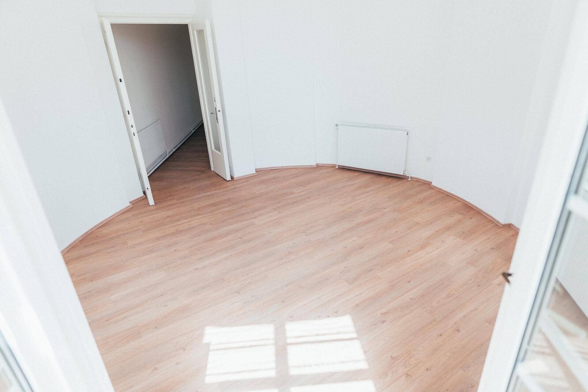 Geräumiger Raum mit Laminatboden und weißen Wänden, mit Zugang zu einem sonnigen Balkon.