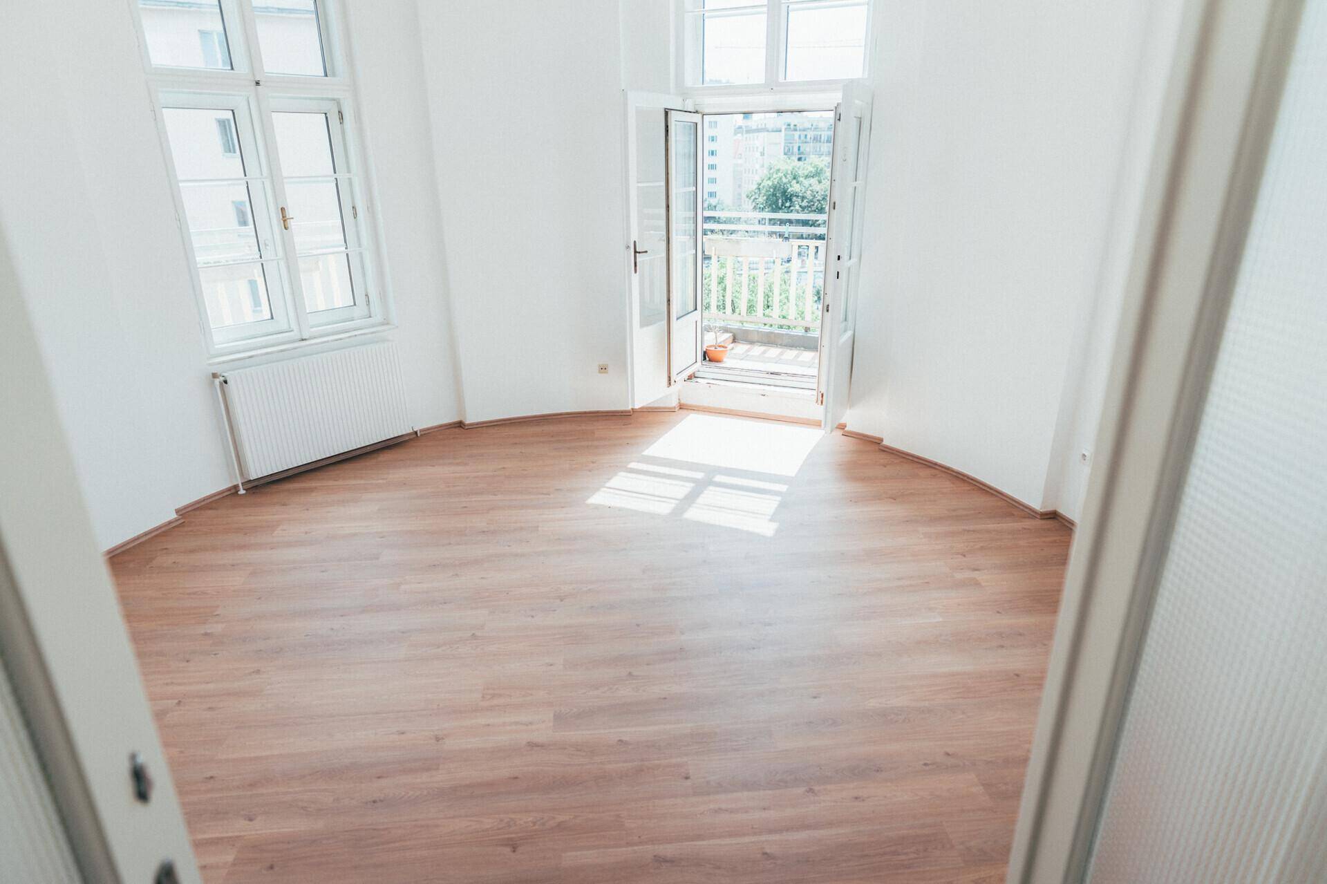 Heller Raum mit Laminatboden und weißen Wänden, mit direktem Zugang zu einem sonnigen Balkon.