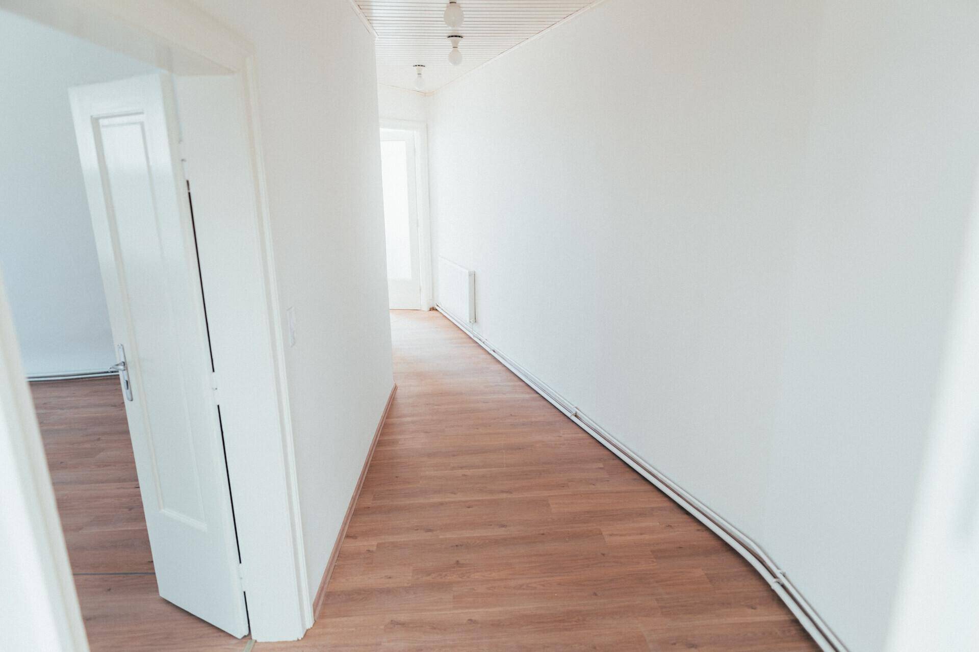 Langer, heller Flur mit Laminatboden und weißen Wänden, der zu weiteren Räumen führt.
