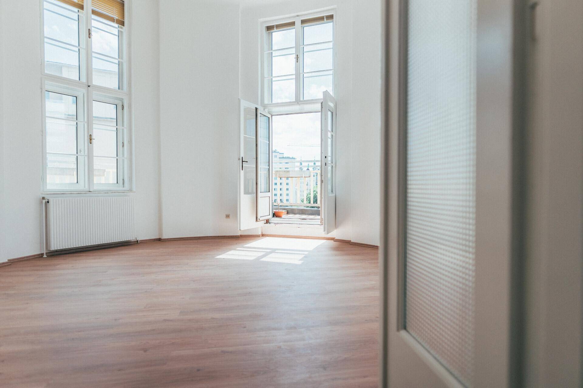 Heller Raum mit Laminatboden und weißen Wänden, mit Zugang zu einem sonnigen Balkon.