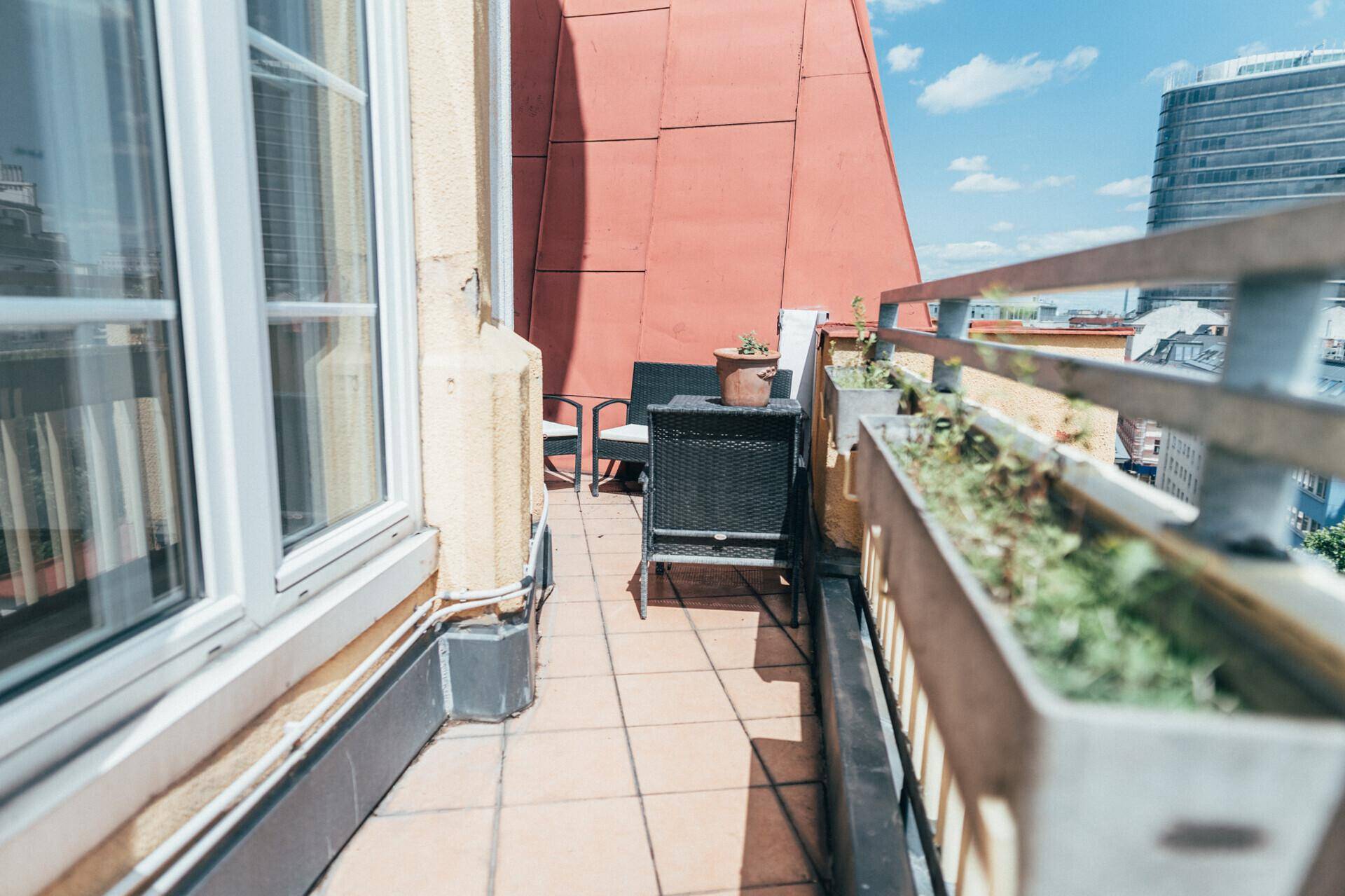 Schmaler Balkon mit Fliesenboden und Sitzgelegenheiten, angrenzend an ein großes Fenster.