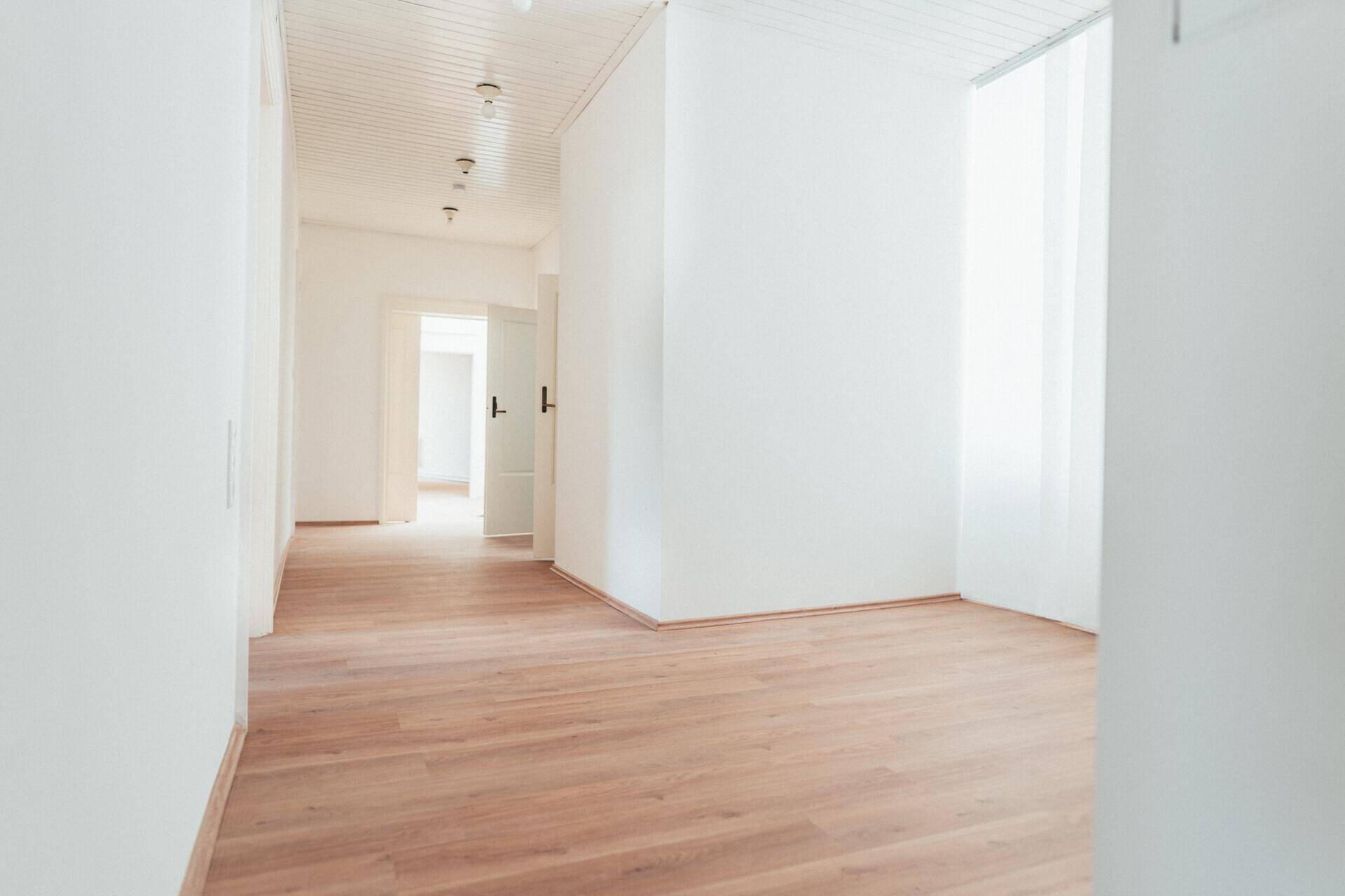 Heller Flur mit Laminatboden, weißen Wänden und einer Holzlamellendecke, führt zu weiteren Räumen.