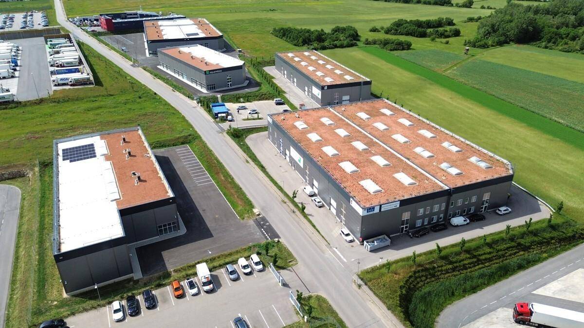 Luftaufnahme eines modernen Gewerbegebiets mit mehreren Gebäuden, Gründächern und Photovoltaikanlagen, umgeben von grünen Feldern.