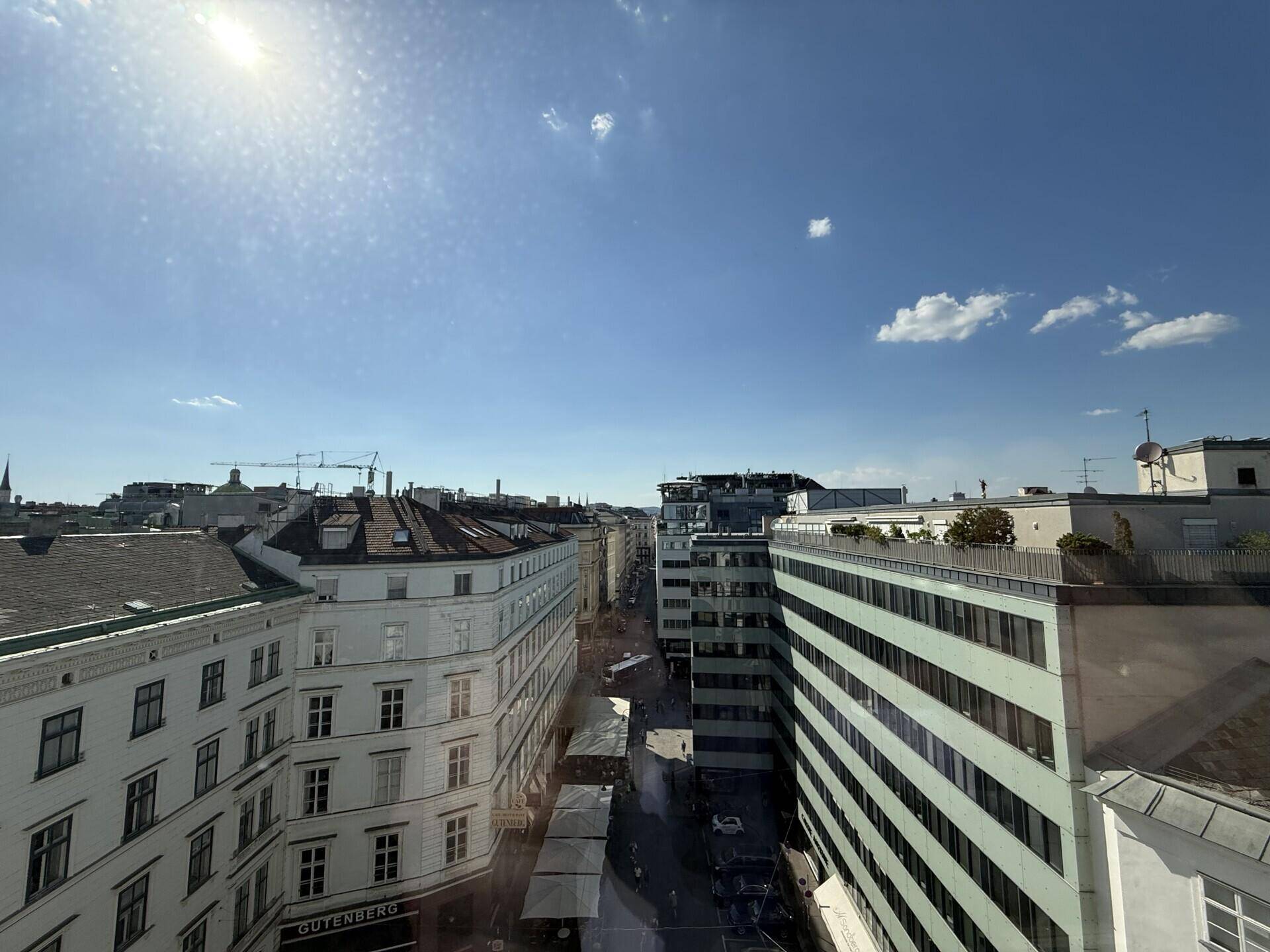 Weitblick über eine belebte Stadtstraße mit Gebäuden unter einem hellen, sonnigen Himmel.