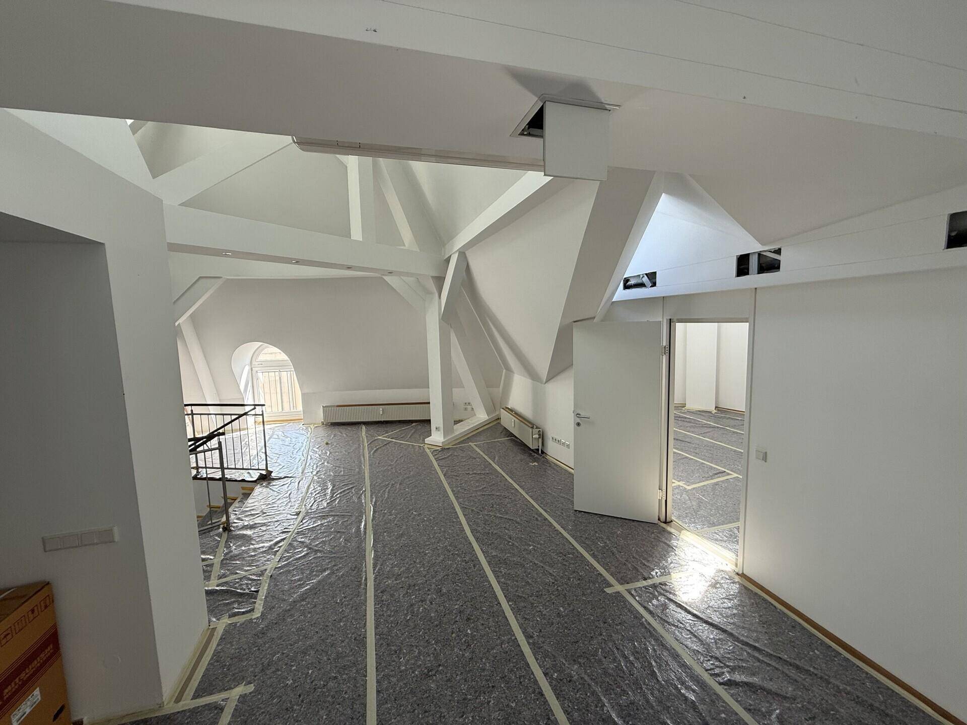 Großer, offener Raum im Dachgeschoss mit sichtbaren Holzbalken und schrägen Decken, derzeit im Umbau.