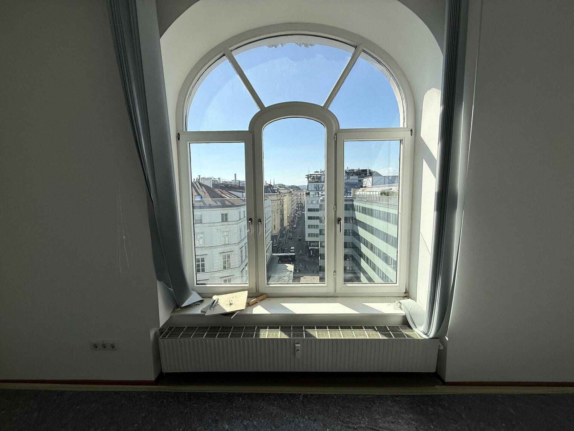 Detailansicht eines großen Rundbogenfensters mit Blick auf die Stadt und die umliegenden Gebäude.