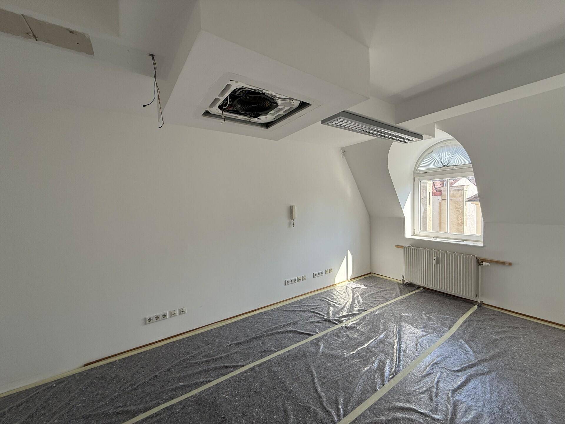 Renovierungsbedürftiger Raum mit schräger Decke, Fenster und Bodenschutzfolie, bereit für den Ausbau.