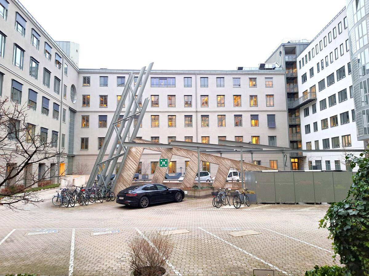 Innenhof mit Parkplätzen, Fahrradständern und moderner Überdachung zwischen den Gebäuden.