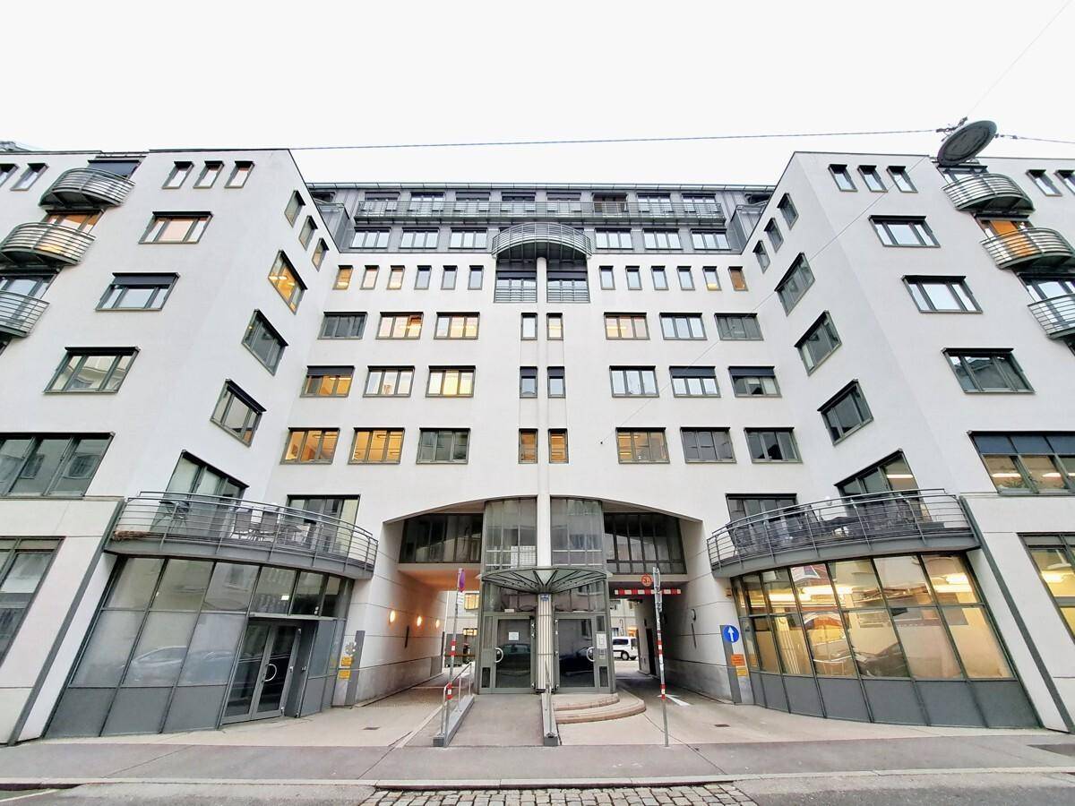 Moderne Gebäudefassade mit vielen Fenstern, Balkonen und einem überdachten Eingangsbereich.