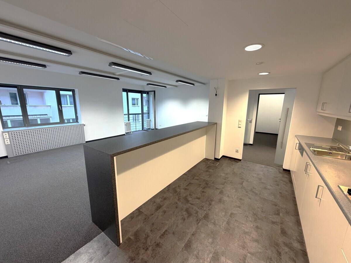 Geräumiges Büro mit integrierter Küchenzeile und Blick auf umliegende Gebäude.