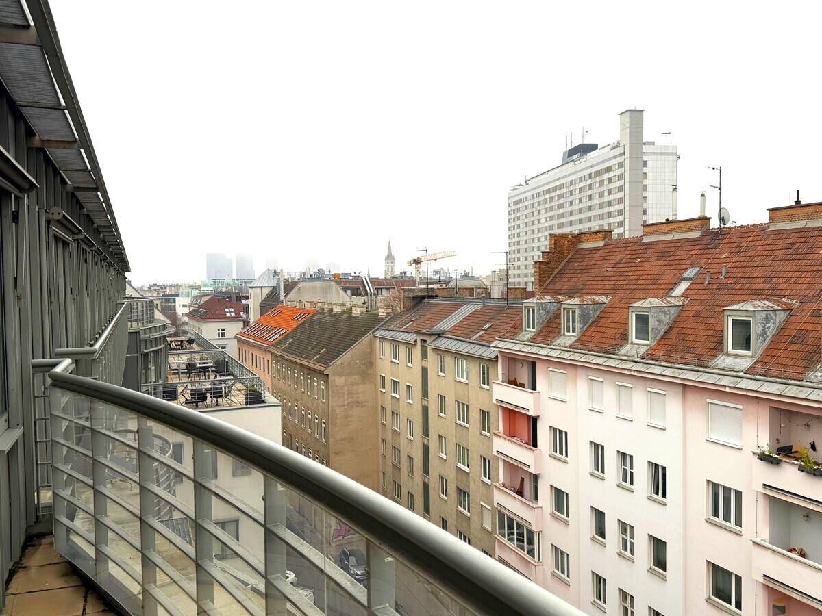 Weitläufiger Stadtblick von einem Balkon mit Blick auf Dächer und umliegende Gebäude.