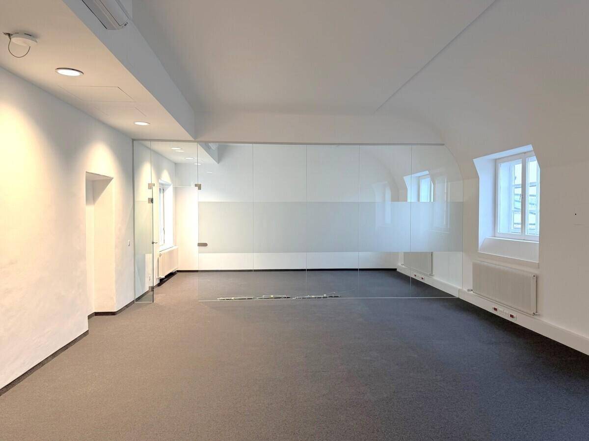 Heller, leerer Büroraum mit Teppichboden und einer modernen Glaswand als Raumteiler.