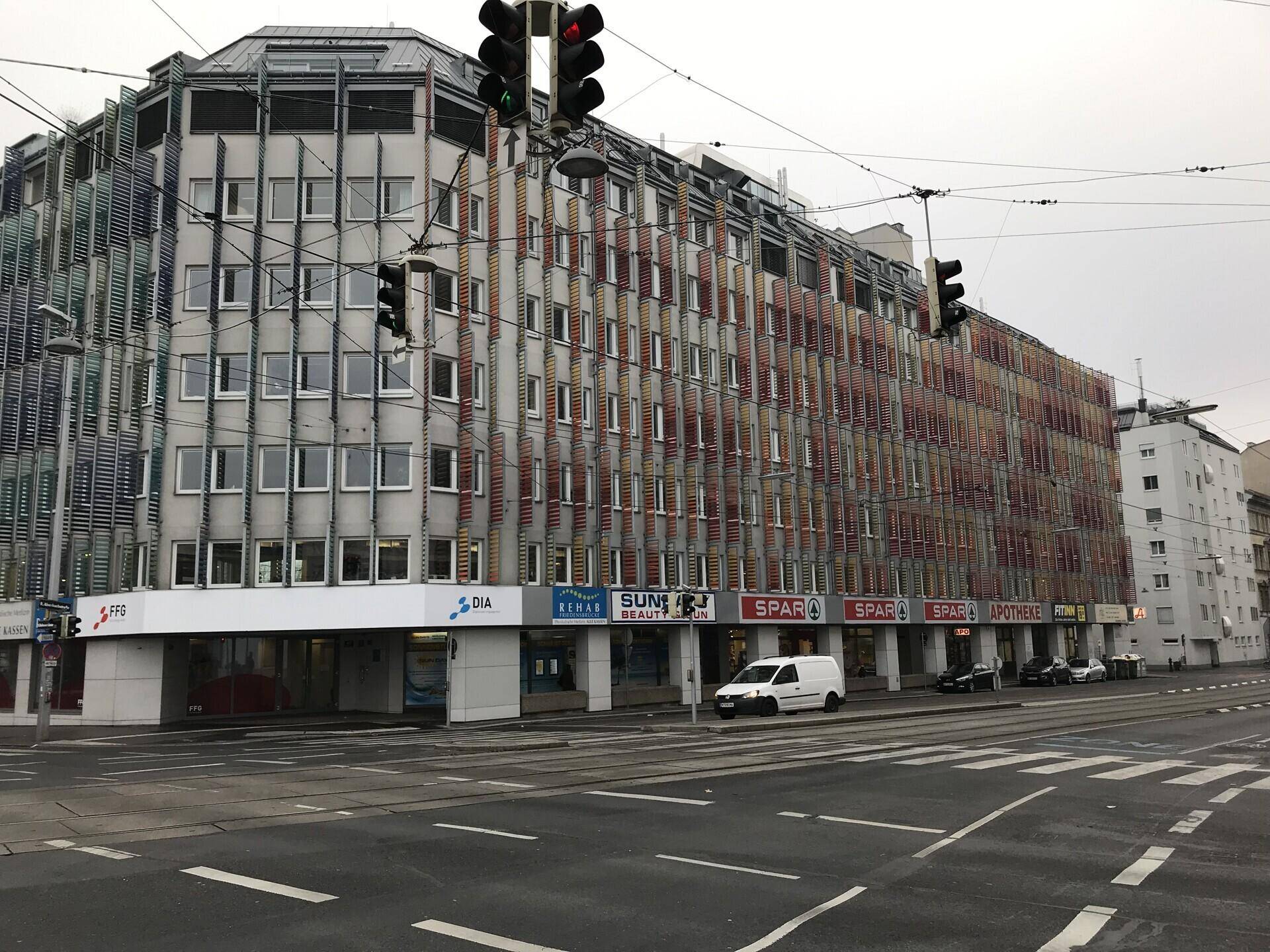 Ansicht des modernen Geschäftsgebäudes an einer städtischen Kreuzung mit Geschäften im Erdgeschoss und vielen Fenstern.