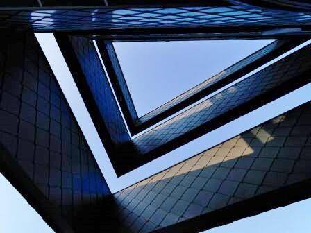 Abstrakte Ansicht der modernen, kantigen Architektur eines Gebäudes, die den Himmel durch die Struktur zeigt.
