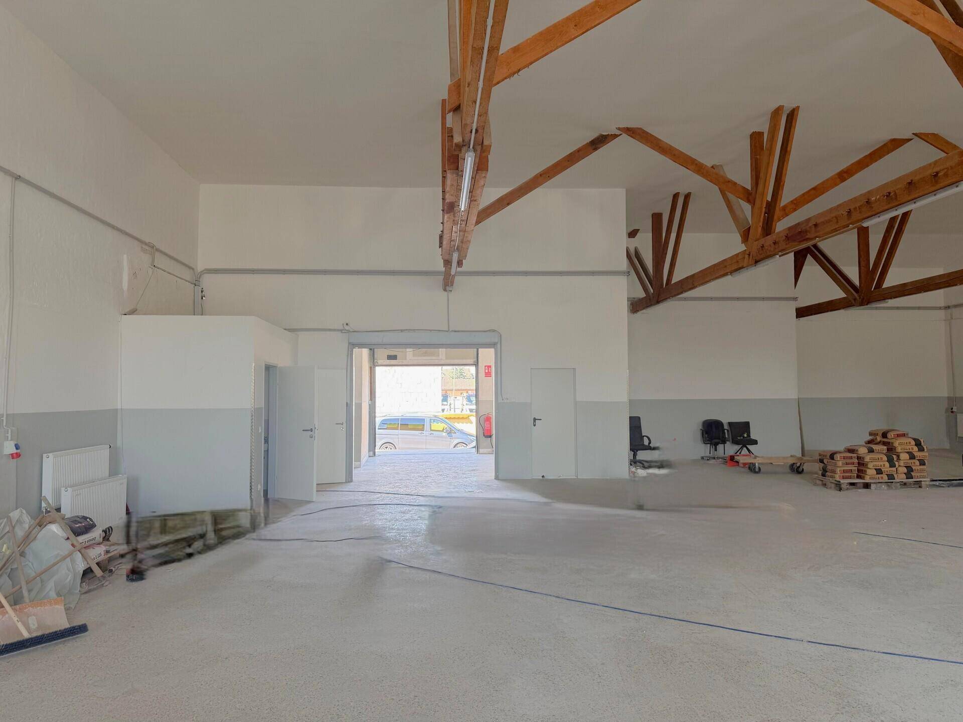 Geräumige Lagerhalle mit hohen Decken, Holzbalken und einem großen Rolltor zum Außenbereich.