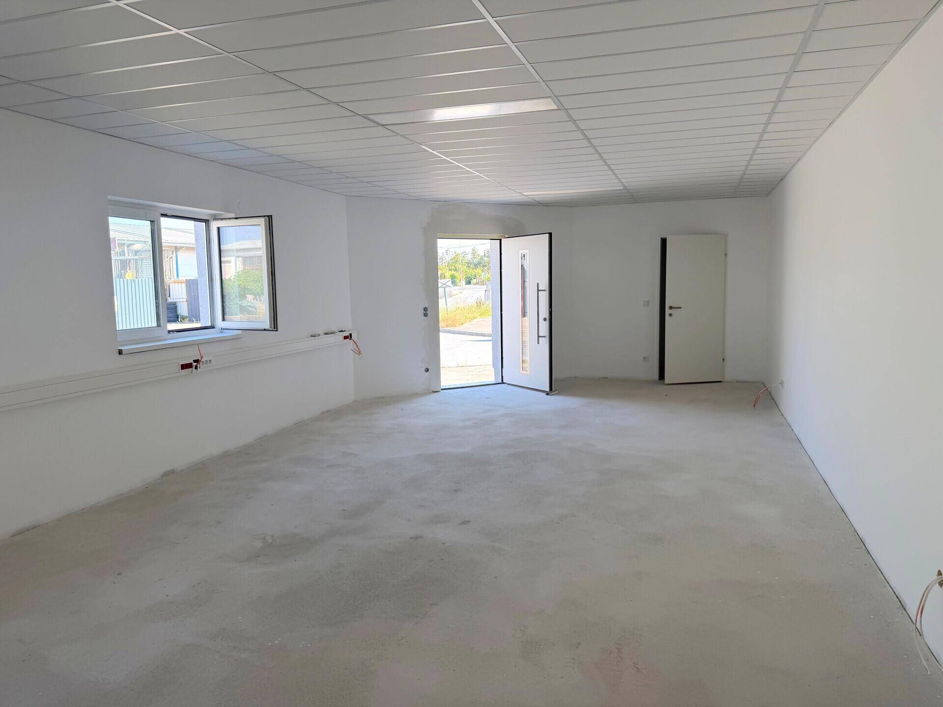 Geräumiger, heller Innenraum mit Fenstern, abgehängter Decke und zwei Türen, bereit zum Ausbau.