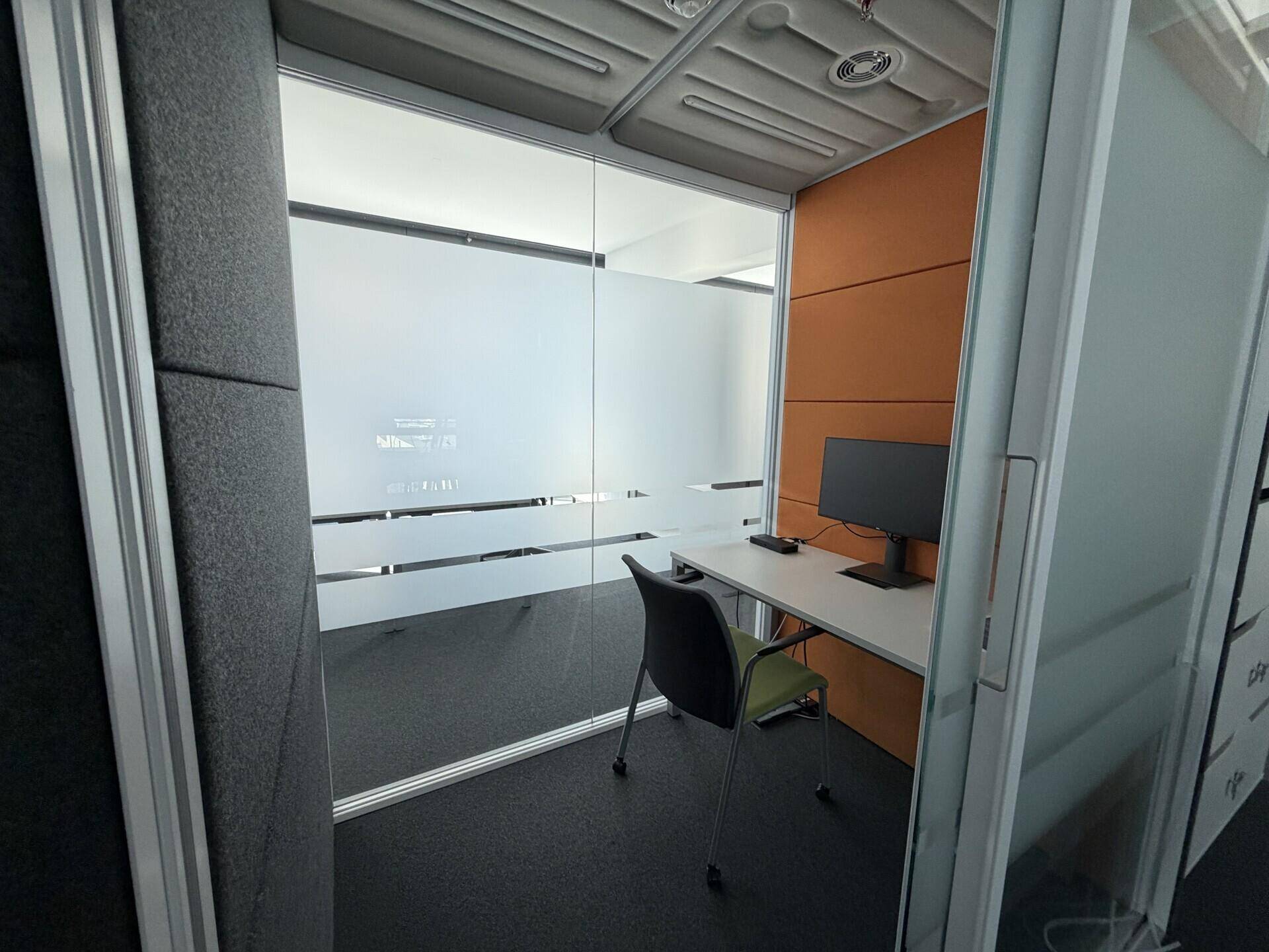 Kleiner, privater Arbeitsbereich oder Telefonzelle mit Schreibtisch und Stuhl, umgeben von schallabsorbierenden Wänden.