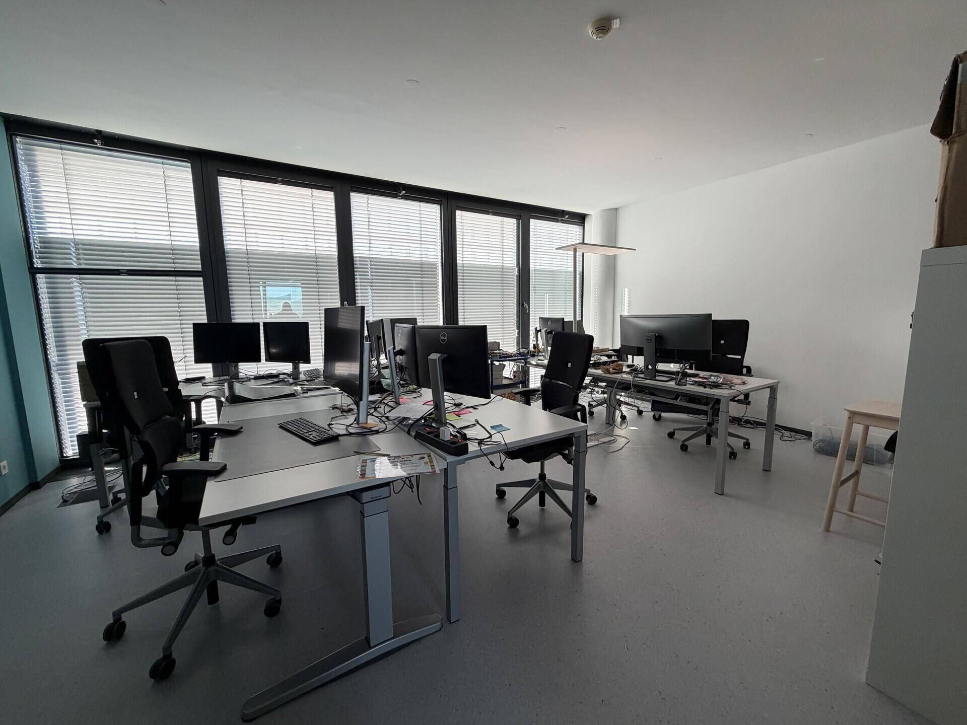 Großes, offenes Büro mit vielen Arbeitsplätzen, großen Fenstern und Jalousien.