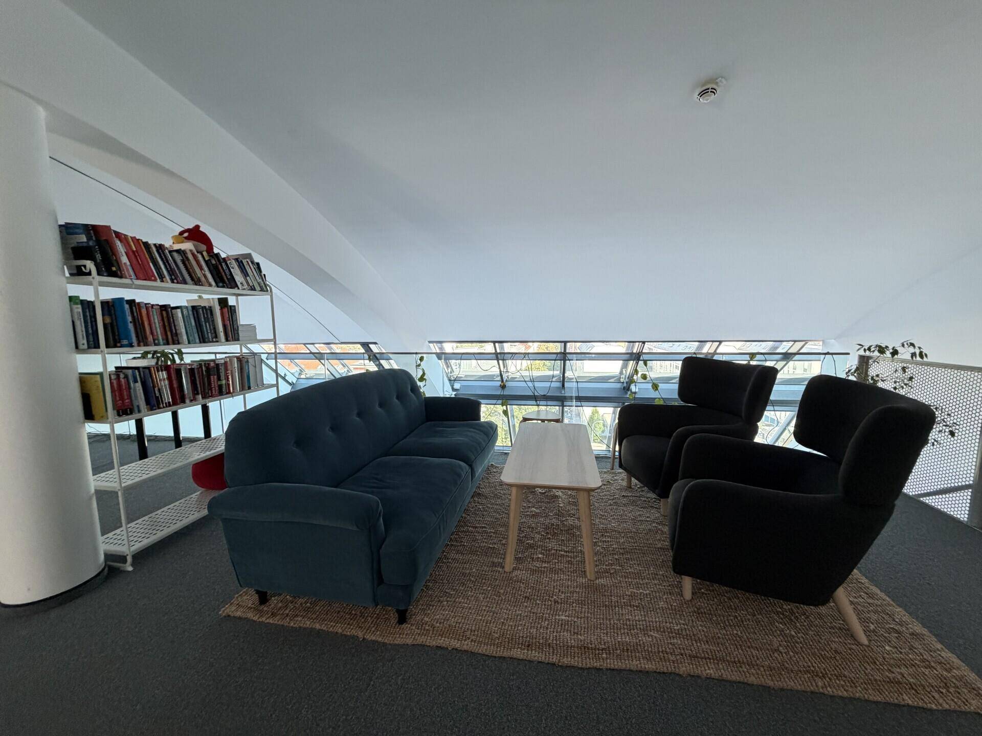 Gemütlicher Loungebereich auf einer oberen Ebene mit Sofa, Sesseln und Blick auf die Stadt durch große Fenster.