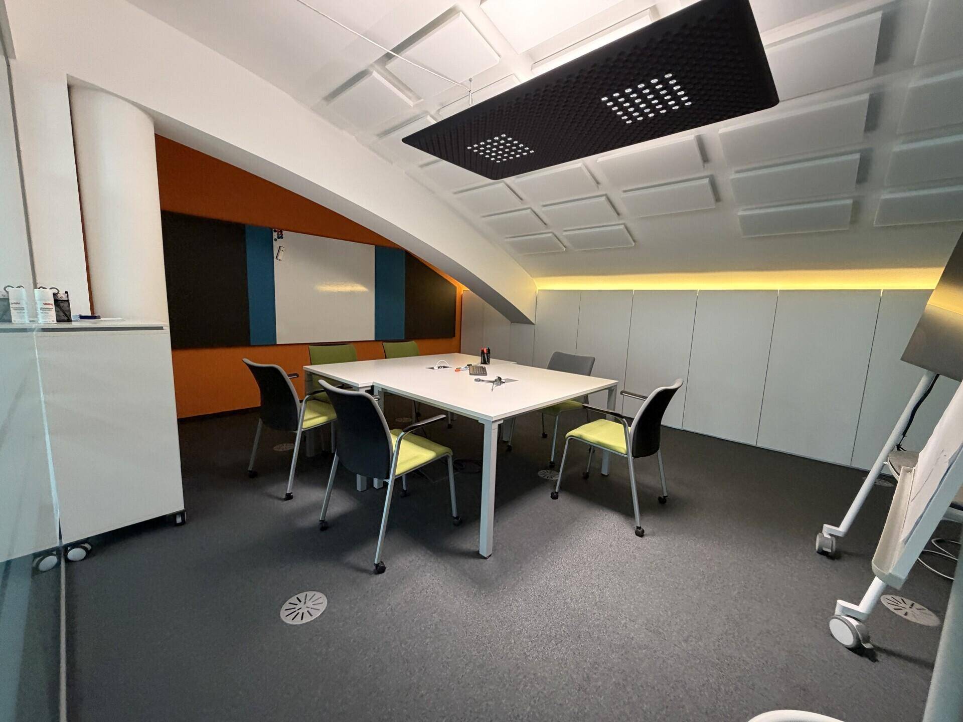 Moderner Konferenzraum mit großem Tisch, Stühlen und schallabsorbierenden Deckenplatten.