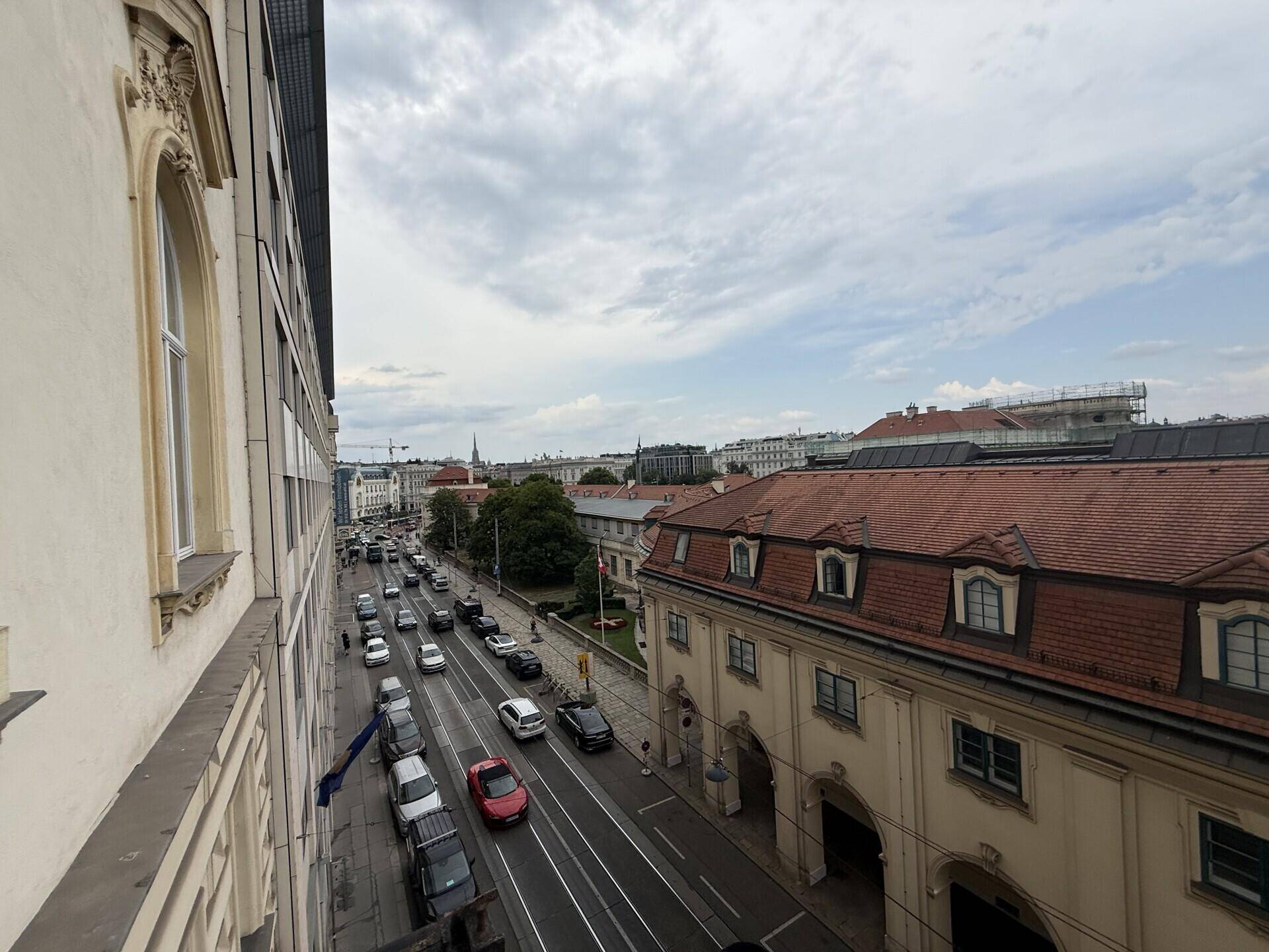 Blick von oben auf eine belebte Straße mit Autos und historischen Gebäuden entlang der Fahrbahn.