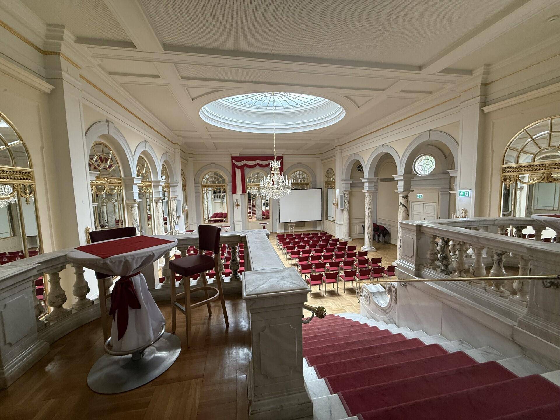 Prächtiger Konferenzsaal mit hohen Decken, Kronleuchter und rotem Teppich auf der Treppe.