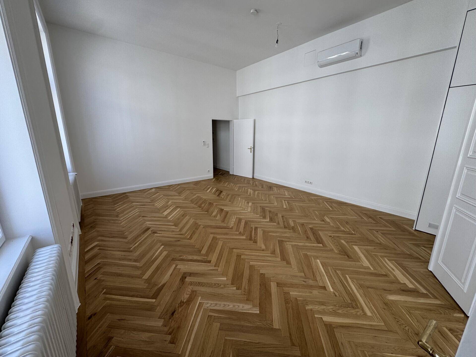 Geräumiger Raum mit elegantem Fischgrätparkett und installierter Klimaanlage an der Wand.
