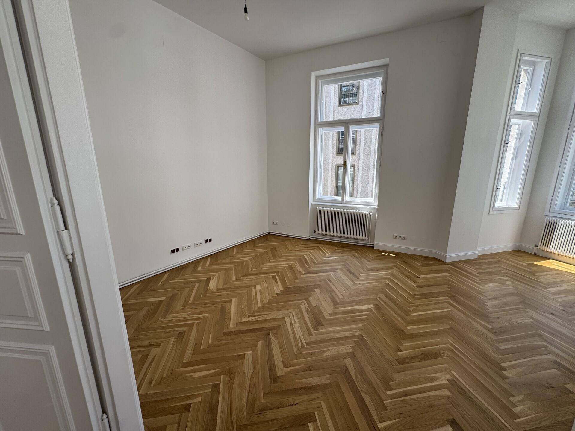 Heller Raum mit Fischgrätparkett und Fenstern, die einen Blick auf die Stadt bieten.