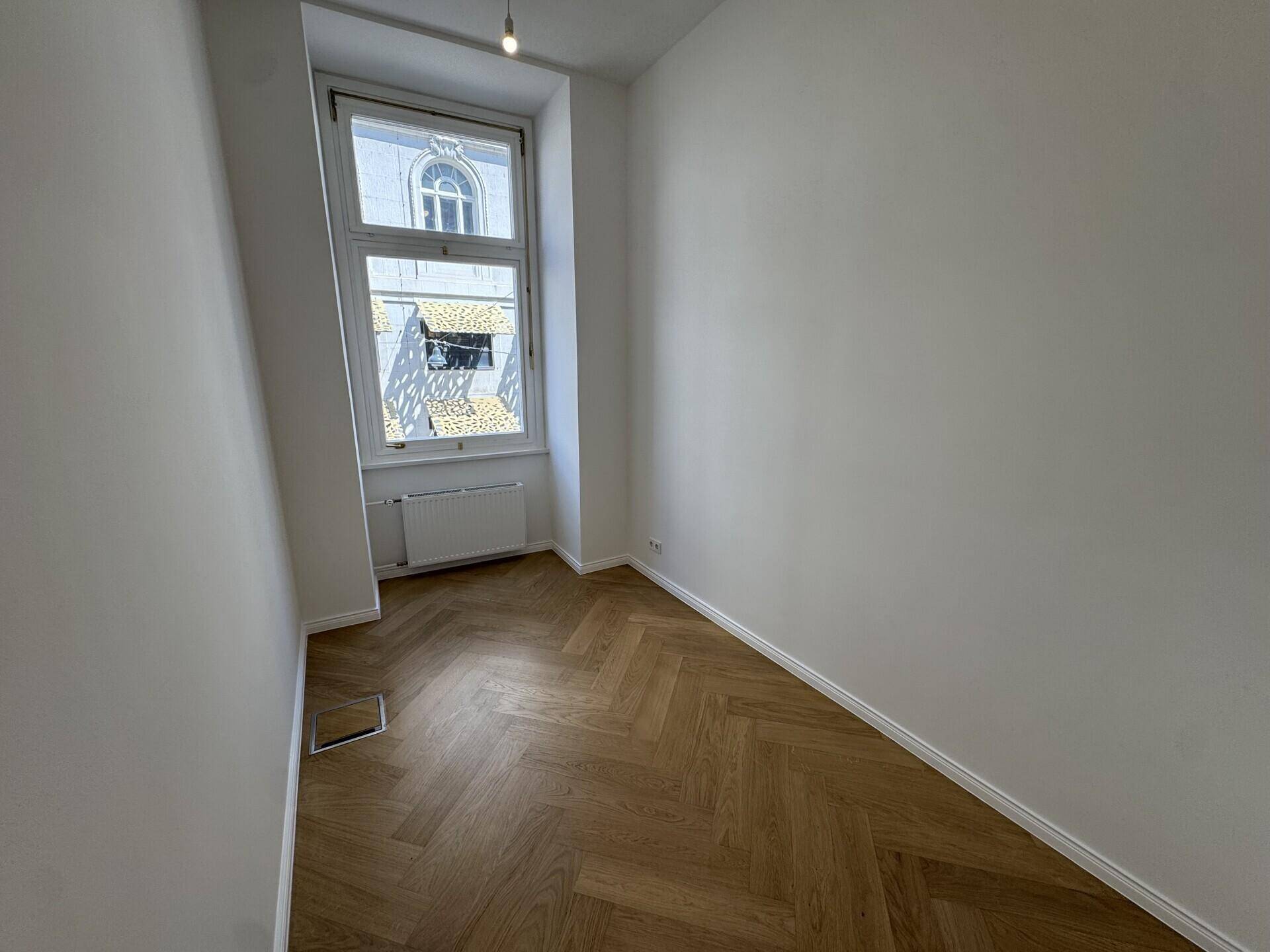 Kleiner, heller Büroraum mit Fischgrätparkett und einem hohen Fenster.