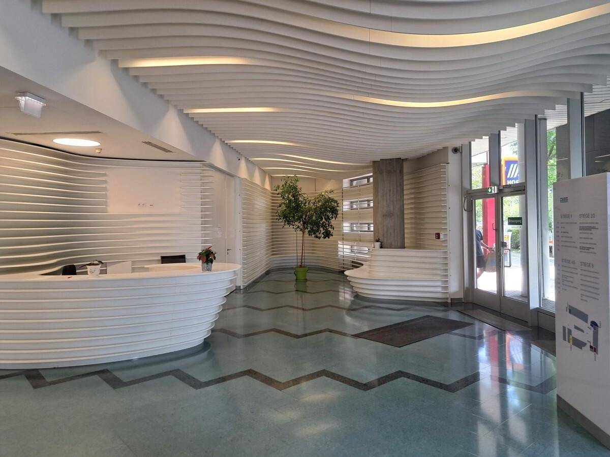 Elegante Lobby mit geschwungenen weißen Empfangstheken, Wellendecke und gemustertem Boden.