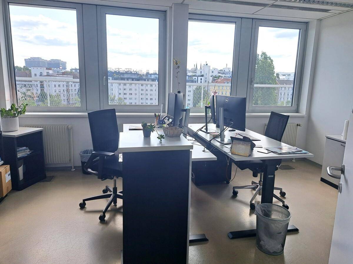 Heller Büroraum mit mehreren Arbeitsplätzen, großen Fenstern und Blick auf die Umgebung.