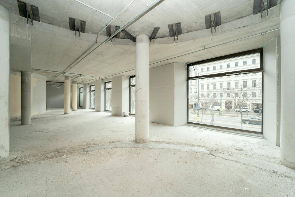 Großer, offener Büroraum im Rohbau mit Betonsäulen und Blick auf die Stadt.