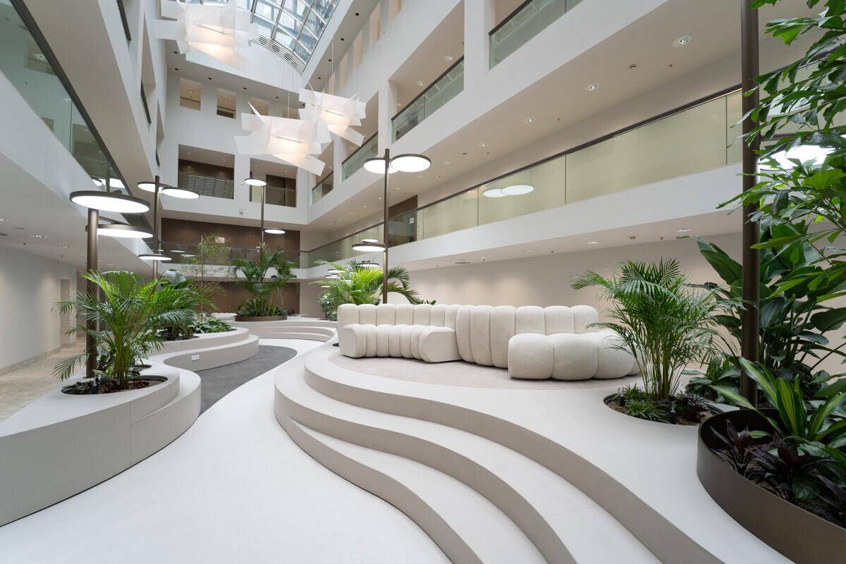 Großzügiges Atrium mit geschwungenen Sitzgelegenheiten, Pflanzen und viel Tageslicht.