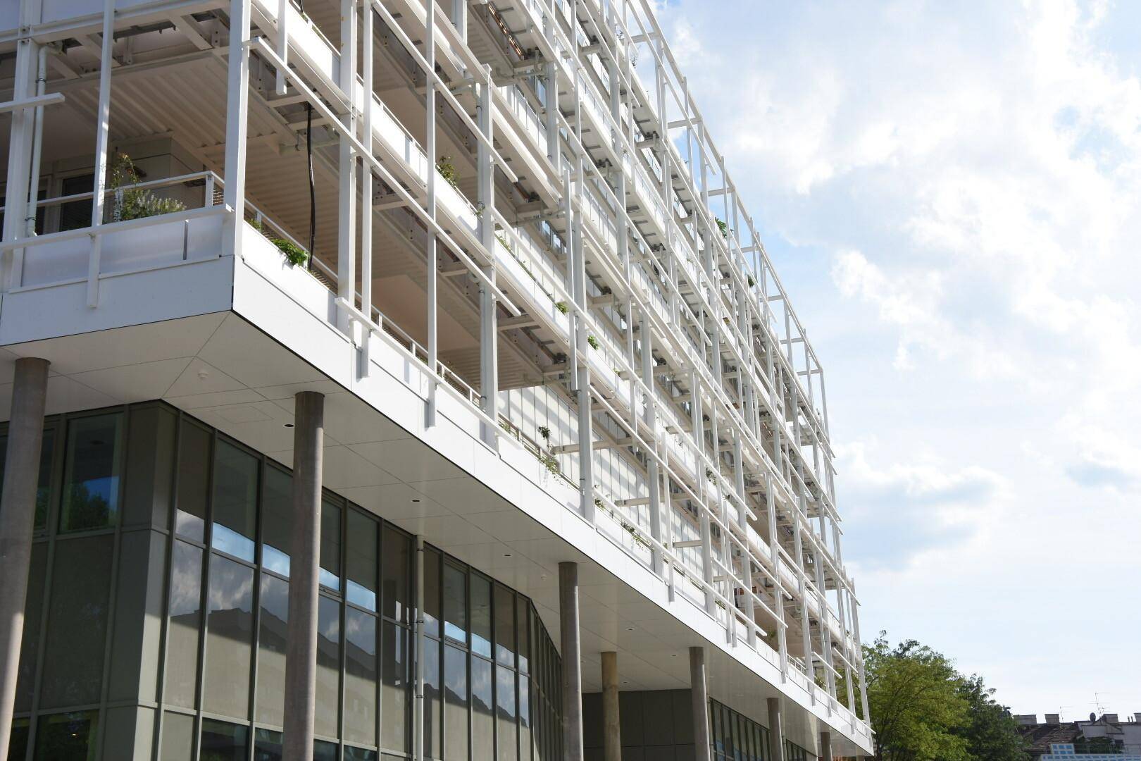 Eckansicht des Gebäudes mit großer Glasfassade im Erdgeschoss und darüberliegenden Etagen.