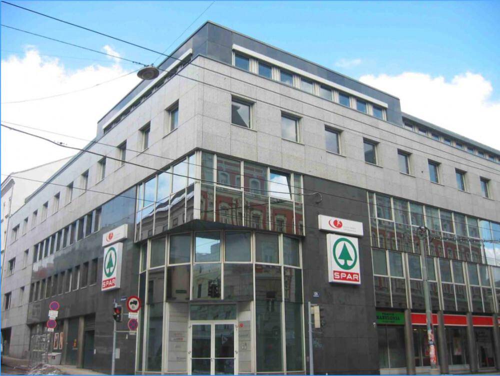 Geschäftsgebäude mit moderner Fassade, großen Fenstern und einem Supermarkt im Erdgeschoss an einer städtischen Straße.
