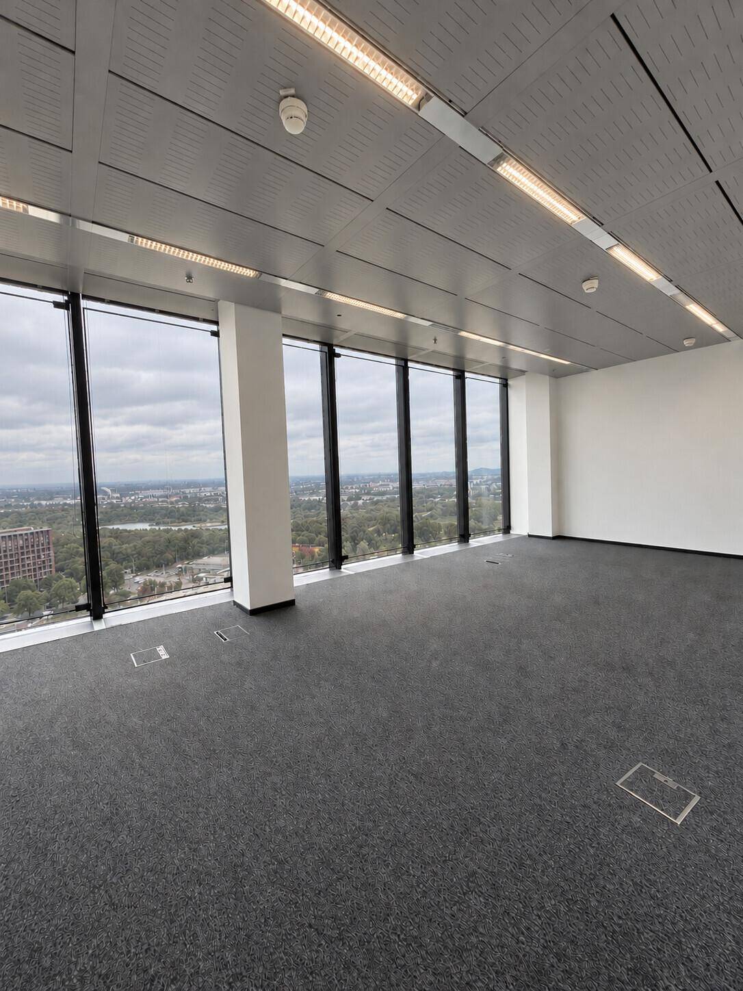 Leerer Büroraum mit Teppichboden, großen Fenstern und weitem Blick über die Stadt.