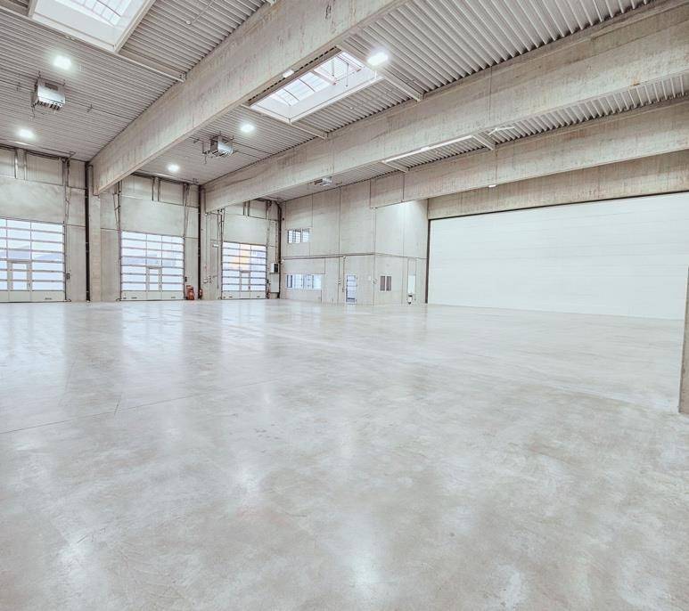 Geräumige Lagerhalle mit hohen Decken, Betonboden, Oberlichtern und großen Rolltoren.
