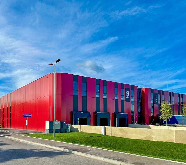 Modernes Industriegebäude mit auffälliger rot-schwarzer Fassade, mehreren Laderampen und Grünflächen.