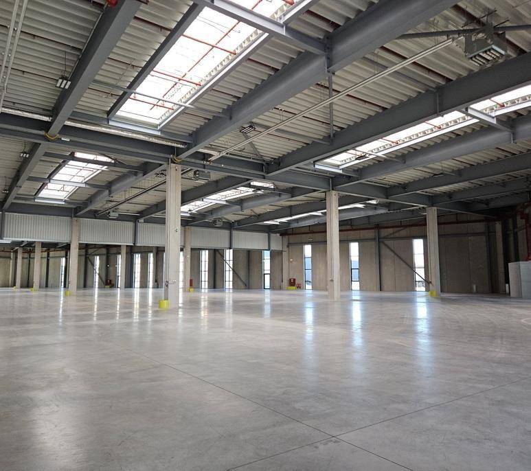 Geräumige, leere Lagerhalle mit hohen Decken, Betonboden und natürlichem Licht durch Oberlichter.