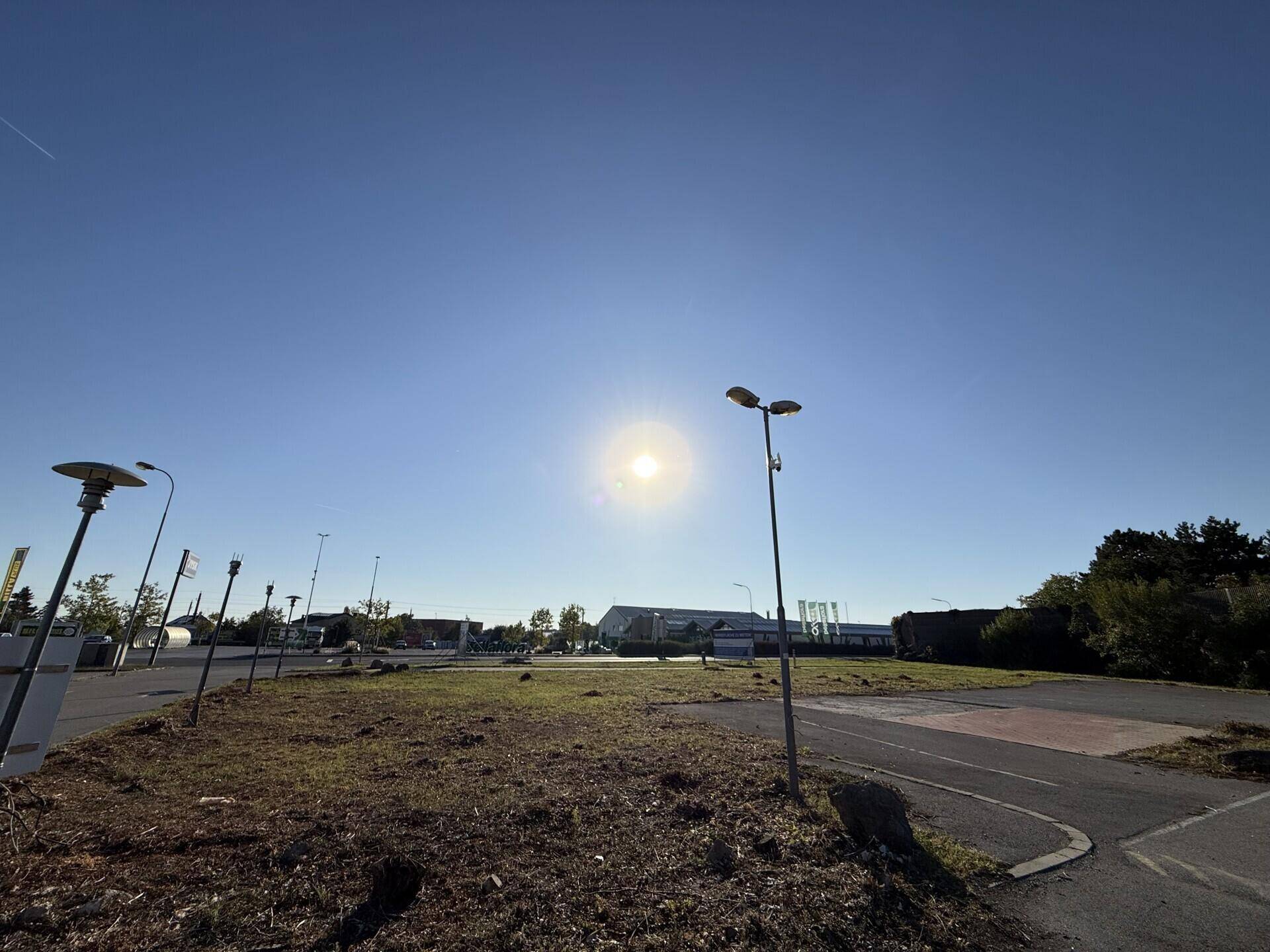 Eine sonnige Außenansicht mit einer Grasfläche, Asphaltwegen und Straßenlaternen unter einem klaren blauen Himmel.
