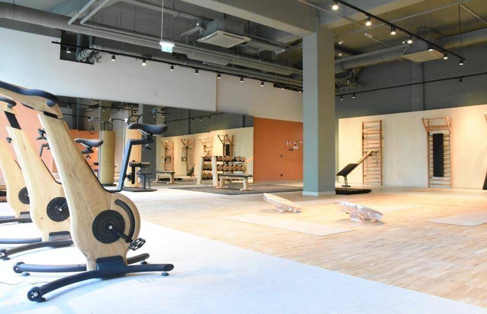 Geräumiger Fitnessraum mit Holzboden, modernen Trainingsgeräten und offener Deckenkonstruktion für sportliche Aktivitäten.