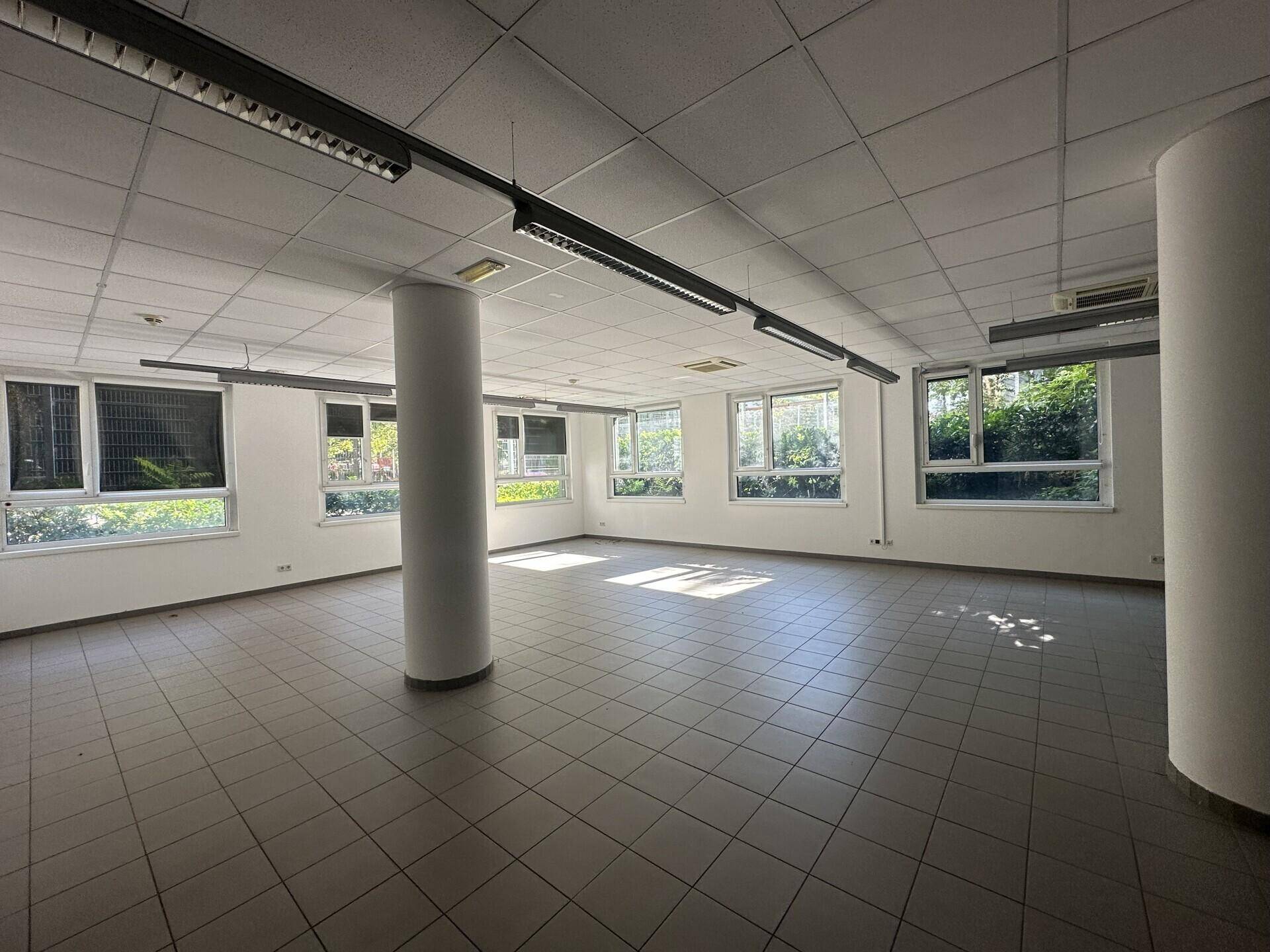 Geräumiger Bürobereich mit Fliesenboden, runden Säulen und zahlreichen Fenstern für optimale Belichtung.