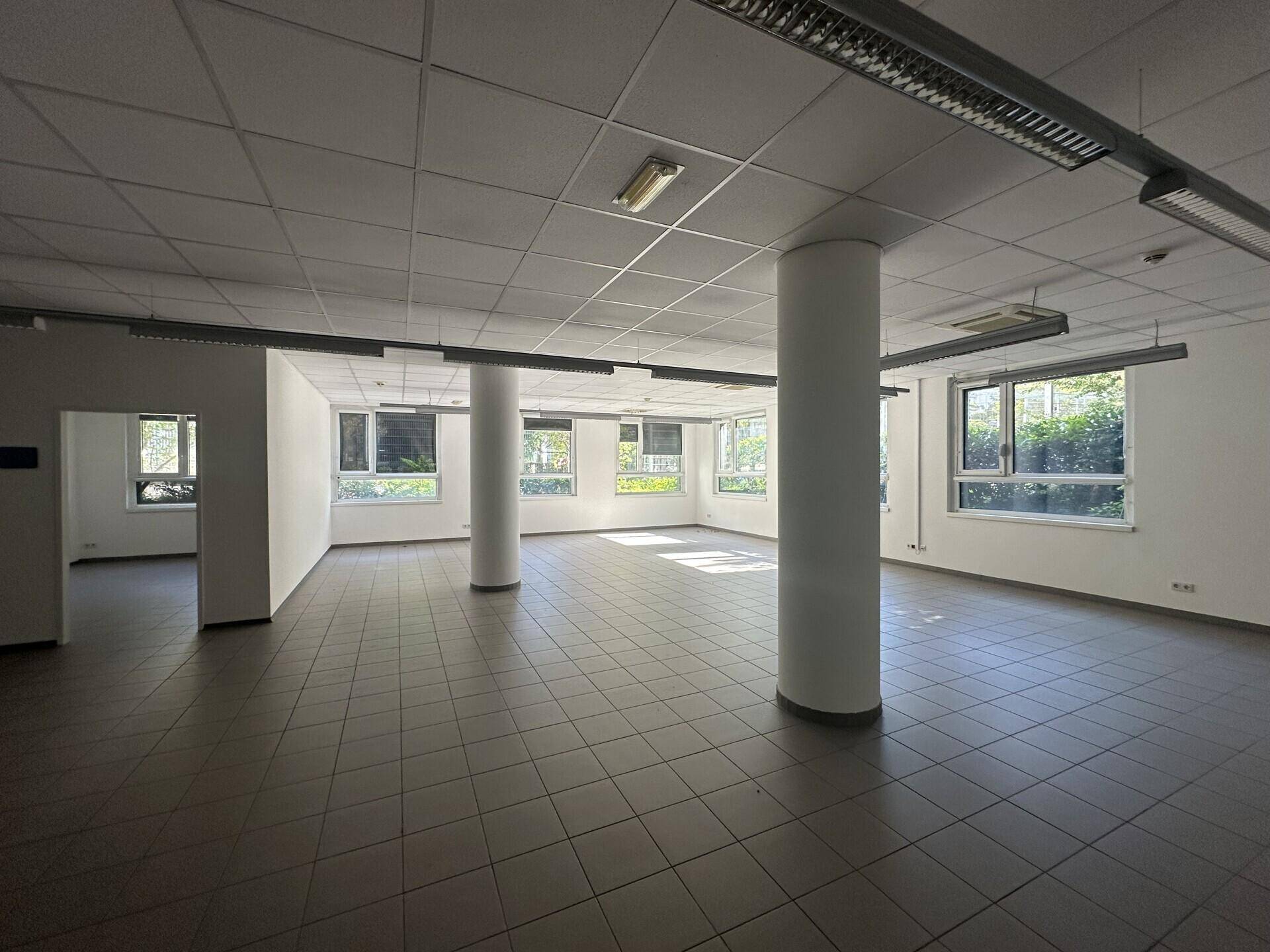 Heller Büroraum mit grauen Fliesen, weißen Säulen und abgehängter Decke, ideal für flexible Gestaltung.